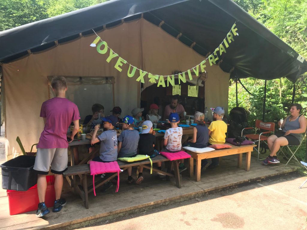 Visuel d'un goûter d'anniversaire, grande tente à la campagne avec des enfants partageant un goûter d'anniversaire.